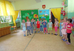 Dzieci w kolorowych ubrankach stoją ustawione w półkolu.